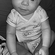 Liyam participe au concours pour gagner de l'argent avec cette photo : baby, infant, child, onesie, cute, hands, feet, smile, face, eyes, sitting, clothing, pattern, text_on_clothing, indoors, blanket, black_and_white, person, portrait, happy