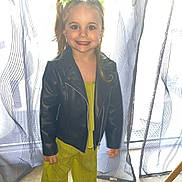 Ilyana a rejoint le concours — aidez-le/la à gagner de superbes lots ! child, girl, smiling, leather_jacket, green_clothing, hair_accessories, curtains, indoor, carpet, window, standing, happy, portrait, fashion, person, cute, toddler, bright_colors, casual, home