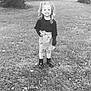 child, girl, smiling, pigtails, outdoor, grass, trees, fence, black_and_white, boots, skirt, bow, long_sleeve, happy, standing, nature, leaves, portrait, person, daytime
