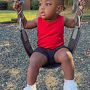 Taliyah is registered to the contest to win money with this photo: child, toddler, baby, swing, playground, outdoor, portrait, sitting, curious, serious_expression, red_shirt, black_shorts, white_shoes, pigtails, natural_light, suburban, trees, house, gravel, playtime