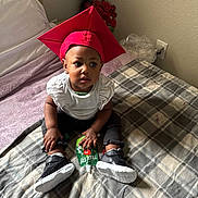 Taliyah is registered to the contest to win money with this photo: baby, child, infant, graduation_cap, red_hat, portrait, sitting, bedroom, bed, blanket, sneakers, shoes, white_shirt, black_pants, snack_pouch, indoors, flowers, lamp, happy, photography