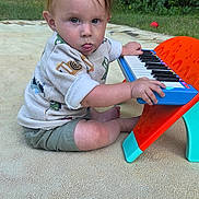 Micah is registered to the contest to win money with this photo: toddler, child, outdoor, toy_keyboard, grass, greenery, playtime, cute, tongue_out, shorts, sweater, sitting, young_child, nature, daylight, fun, expression, person, summer, playful