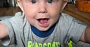 Micah is registered to the contest to win money with this photo: toddler, child, smiling, happy, indoor, living_room, shirt, dinosaur, text_on_clothing, person, face, eyes, hair, carpet, furniture, television, home, candid, portrait, baby