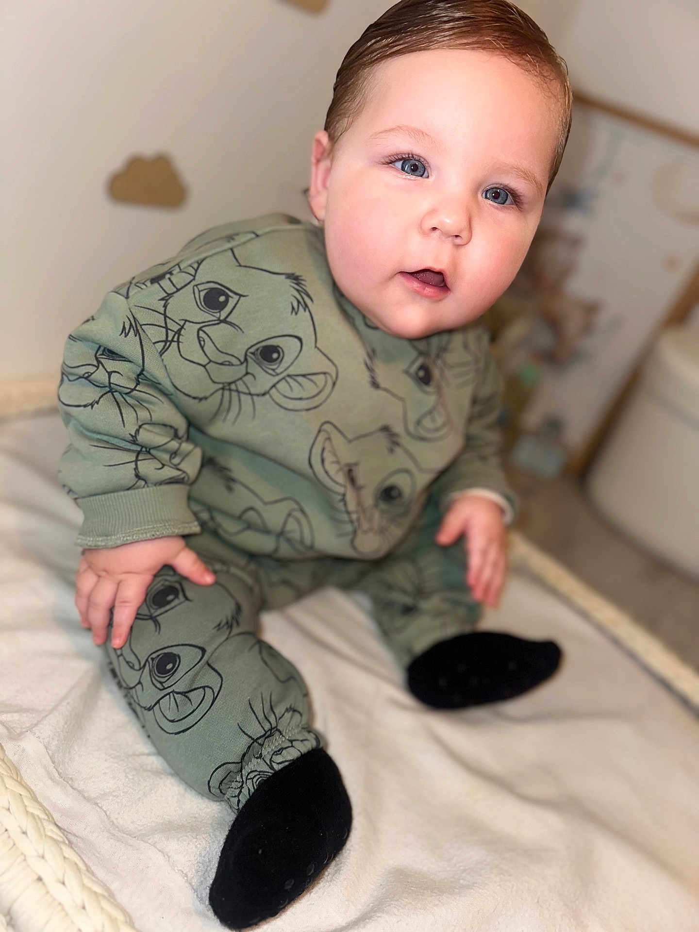 Menzo participe au concours pour gagner de l'argent avec cette photo : baby, child, infant, blue_eyes, green_outfit, lion_print, sitting, blanket, indoors, cute, soft_lighting, portrait, hand, footwear, black_socks, curious_expression, face, head, young_child, cozy