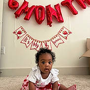 Rhyleigh is registered to the contest to win money with this photo: baby, child, infant, strawberry, red_balloon, birthday, half_birthday, carpet, white_wall, curly_hair, cute, sitting, decorations, celebration, earrings, clothing, indoor, portrait, smiling, young_child