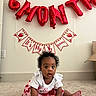 baby, child, infant, strawberry, red_balloon, birthday, half_birthday, carpet, white_wall, curly_hair, cute, sitting, decorations, celebration, earrings, clothing, indoor, portrait, smiling, young_child