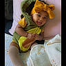 baby, child, smiling, yellow_bow, green_outfit, blanket, pillow, cute, indoors, sitting, happy, sock, furniture, portrait, cozy, person, headwear, infant, tongue_out, soft_toys
