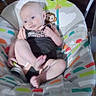 baby, infant, baby_seat, clothing, harley_davidson, indoor, patterned, colorful, face, person, child, seat, cute, expression, skin, foot, hand, monkey_toy, fabric, wood_floor