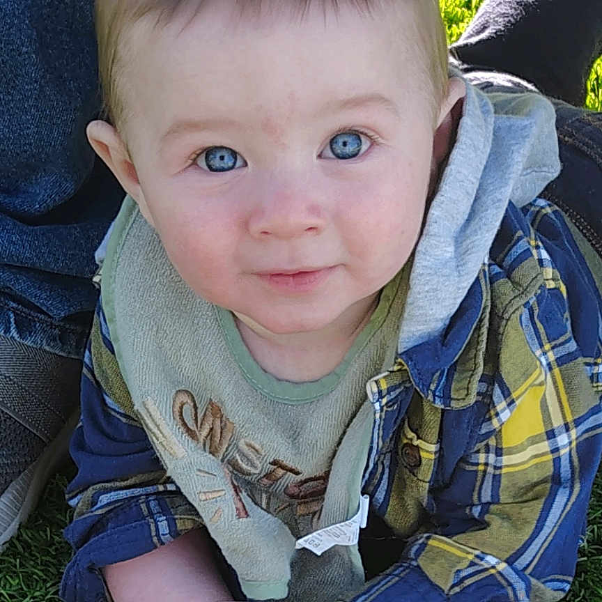 Carter joined the competition — help win amazing prizes! baby, child, infant, portrait, outdoor, grass, smiling, blue_eyes, plaid_shirt, bib, seated, hands, face, head, short_hair, sunlight, lawn, park, cute, photography