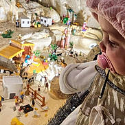 Abigaël a rejoint le concours — aidez-le/la à gagner de superbes lots ! baby, child, close_up, clothing, curious, detailed, diorama, face, figurines, imaginative, indoor, miniature, pacifier, pink_hat, profile, small_animals, soft_lighting, toys, village, warm