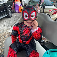 Mateo is registered to the contest to win money with this photo: child, toddler, costume, spiderman, mask, smile, outdoor, bench, halloween, decoration, toy, car, vehicle, holiday, festive, playful, cute, face, clothing, seat