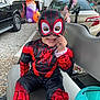 child, toddler, costume, spiderman, mask, smile, outdoor, bench, halloween, decoration, toy, car, vehicle, holiday, festive, playful, cute, face, clothing, seat