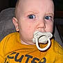 baby, pacifier, yellow_shirt, blue_eyes, face, expression, indoor, child, curious, closeup, portrait, sitting, clothing, infant, person, young_child, cute, head, skin, eyelashes