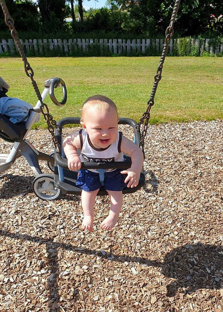 Denis is registered to the contest to win money with this photo: backyard, child, city, fun, grass, human_settlement, lawn, outdoor_play_equipment, park, person, plant, play, playground, public_space, recreation, smile, soil, swing, toddler, tree