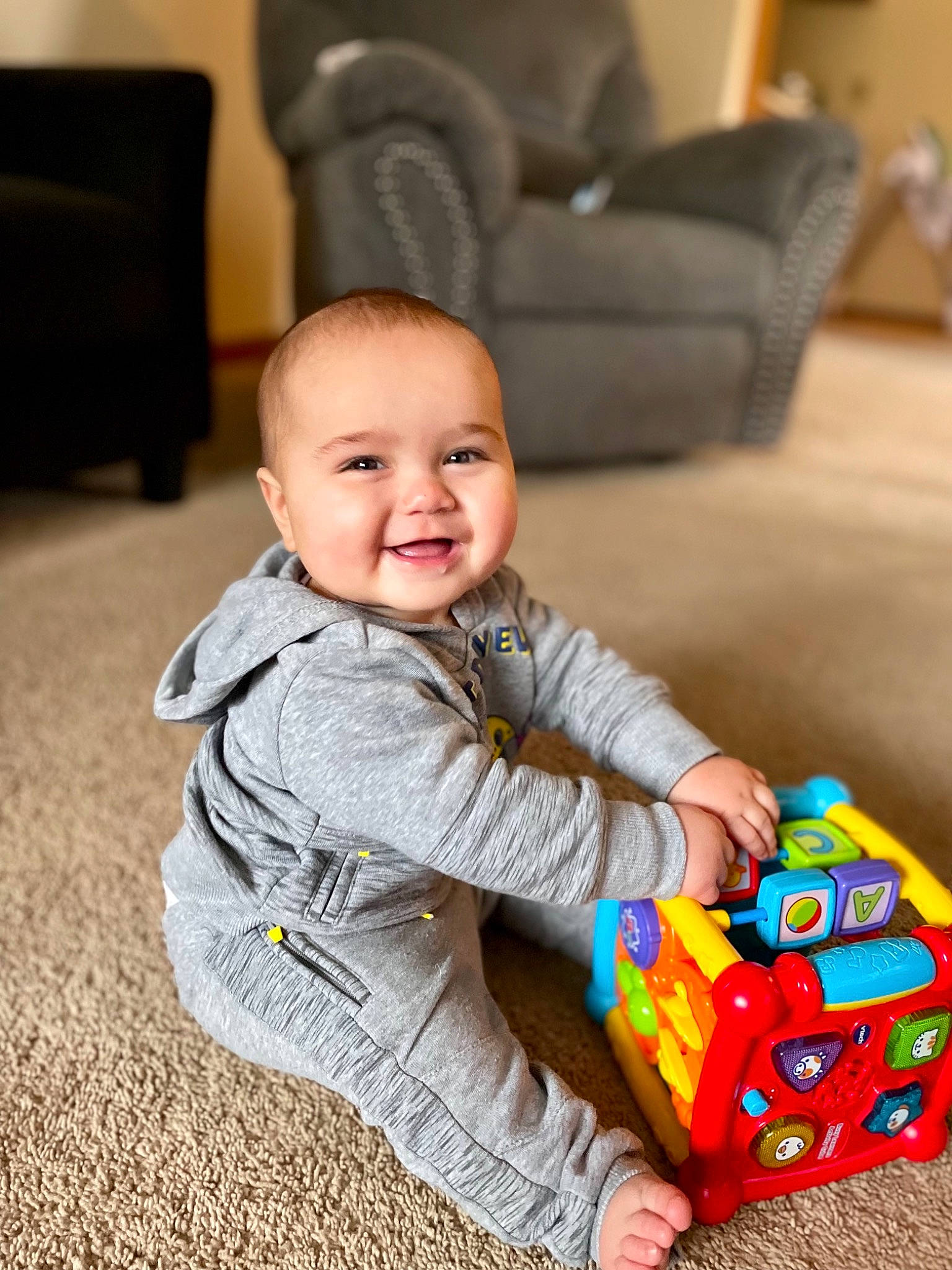 Peter is registered to the contest to win money with this photo: baby, baby_playing_with_toys, baby_toddler_clothing, cheek, child, comfort, couch, floor, flooring, fun, furniture, happy, joy, person, sitting, skin, sleeve, smile, toddler, toy