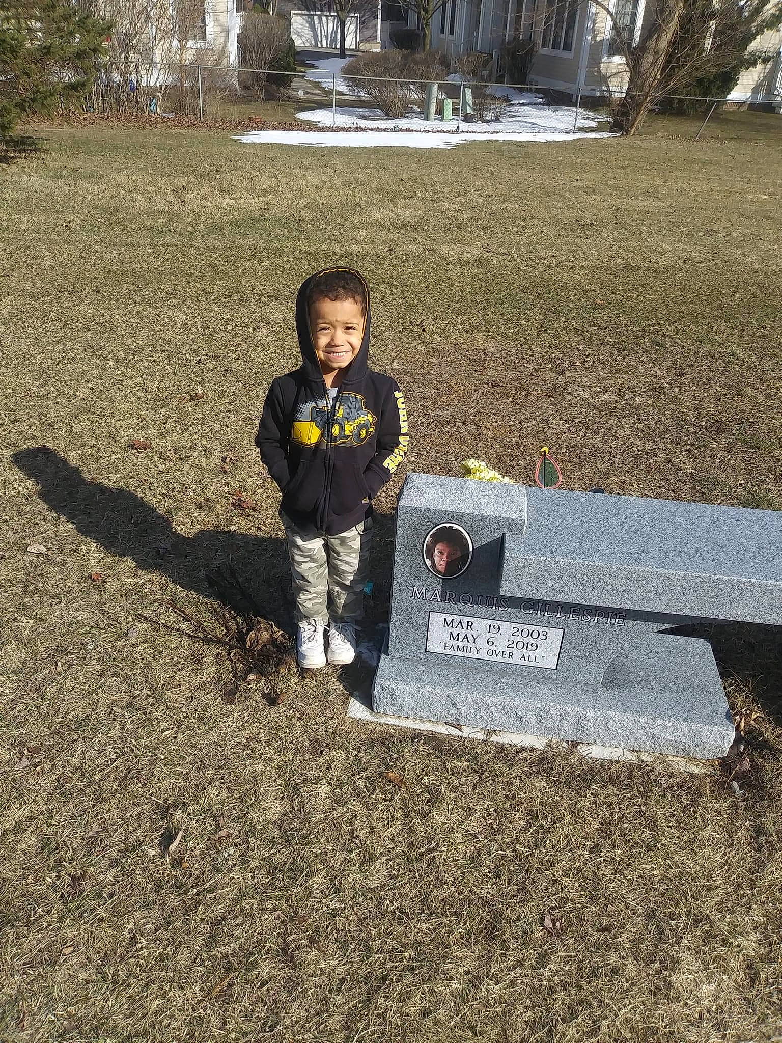 Braxton is registered to the contest to win money with this photo: asphalt, child, city, concrete, grass, hoodie, joy, landscape, person, plant, recreation, road_surface, shadow, sitting, soil, t_shirt, toddler, tree, winter, yard