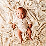 baby, infant, smiling, knitted_clothing, blanket, soft_texture, happy, cute, child, portrait, laying_down, indoor, one_person, human, newborn, face, skin, eyes, expression, warm_color