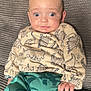 Eden is registered to the contest to win money with this photo: baby, beige_top, blanket, casual_wear, child, clothing, comfortable, cute, dinosaur_print, expression, green_pants, hand, indoor, infant, portrait, sitting, soft_lighting, texture, wide_eyes, young_child