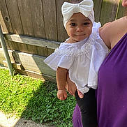Olivia joined the competition — help win amazing prizes! baby, child, headband, white_bow, white_top, black_leggings, person, adult, holding, outdoor, grass, wooden_fence, sunlight, shadow, side_view, smiling, cute, portrait, casual_clothing, greenery