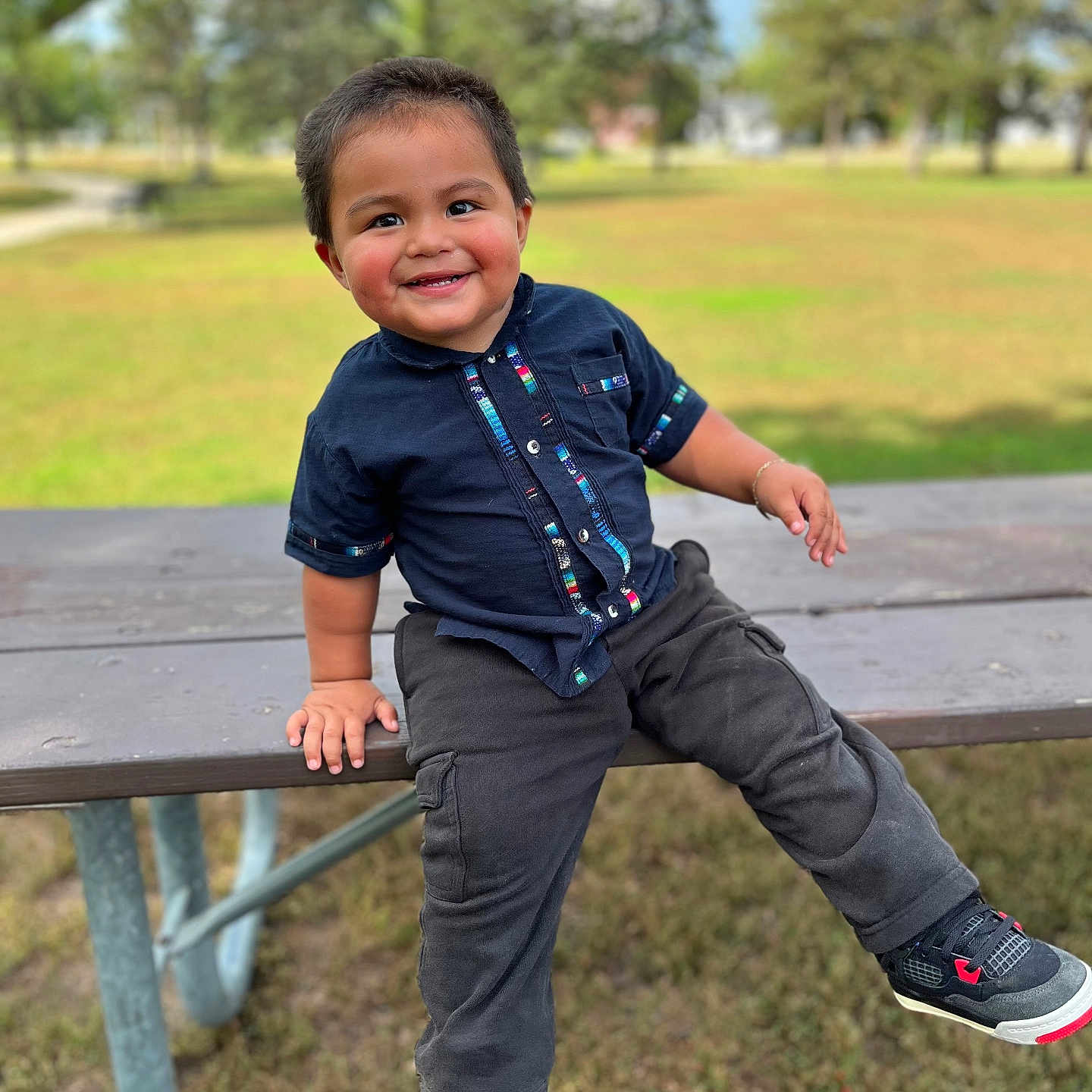 Daniel Alvizures joined the competition — help win amazing prizes! blue_sky, boy, casual_clothing, child, cute, daylight, grass, happy, nature, outdoor, park, picnic_table, playful, short_hair, sitting, smiling, sneakers, toddler, trees, young_child