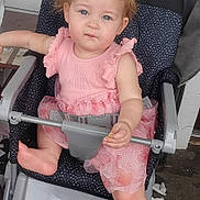 Oaklyn is registered to the contest to win money with this photo: toddler, child, pink_dress, curly_hair, stroller, foot, snack, seat_belt, indoor, expression, face, blue_eyes, barefoot, clothing, person, sitting, hand, hair, pattern, furniture