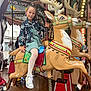 amusement_park, background, carousel, child, clothing, decorative, entertainment, fun, girl, indoors, jacket, lights, playful, pole, reindeer, ride, smile, sneakers, tights, wooden_floor