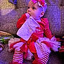 Oaklee is registered to the contest to win money with this photo: baby, child, tutu, bow, headband, striped_leggings, red_clothing, white_tulle, couch, tissue, chewing, sitting, festive, holiday, indoor, cozy, soft_lighting, curious, cute, infant