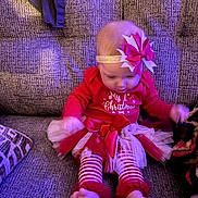Oaklee joined the competition — help win amazing prizes! baby, child, christmas, holiday, red_clothing, striped_leggings, bow_headband, tutu, couch, furniture, indoor, festive, cute, sitting, infant, toddler, soft_lighting, cozy, holiday_outfit, motion_blur