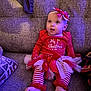 Oaklee is registered to the contest to win money with this photo: baby, child, infant, christmas, holiday_clothing, red_clothing, striped_leggings, tutu, bow, headband, couch, seated, indoors, festive, cute, portrait, soft_lighting, expression, cozy, happy