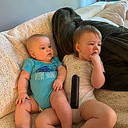 Blakely Parsons is registered to the contest to win money with this photo: toddler, baby, child, couch, blanket, remote_control, onesie, furniture, indoor, sitting, cute, face, skin, hand, foot, expression, comfort, leisure, home, relax