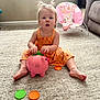 Blakely Parsons joined the competition — help win amazing prizes! toddler, child, toy, piggy_bank, carpet, living_room, orange_dress, plastic_discs, baby_chair, sofa, indoor, playtime, cute, person, young_child, hair_pigtails, floor, colorful, sitting, curious