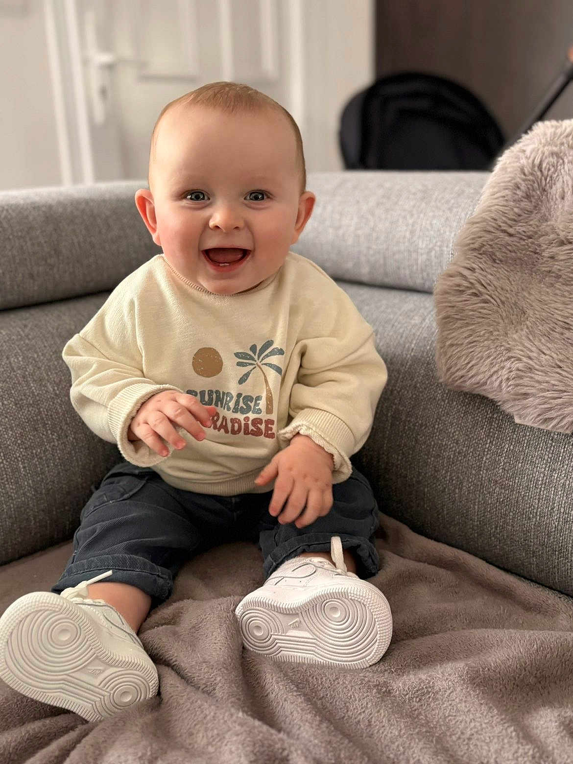 Elyo a rejoint le concours — aidez-le/la à gagner de superbes lots ! baby, infant, smiling, indoor, couch, blanket, sneakers, sweater, palm_tree, graphic_print, happy, portrait, cute, eyes, hands, ears, pillow, soft_texture, stroller, depth_of_field