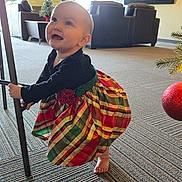 Renesmee is registered to the contest to win money with this photo: baby, child, plaid_dress, barefoot, indoor, carpet, chair_leg, smiling, happy, holiday, christmas_tree, decorations, curious, toddler, person, furniture, window, light, floor, cute
