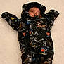 baby, child, cold_weather, colorful, cozy, cute, face, hood, infant, lying_down, outdoor, patterned_clothing, person, playful, smiling, snow, snowsuit, warm, winter, winter_clothing