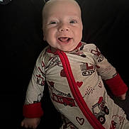 Jackson is registered to the contest to win money with this photo: baby, smiling, infant, onesie, clothing, red_trim, heart_pattern, toy, pacifier, happy, face, person, cute, indoors, child, young, lying_down, expression, cheerful, closeup
