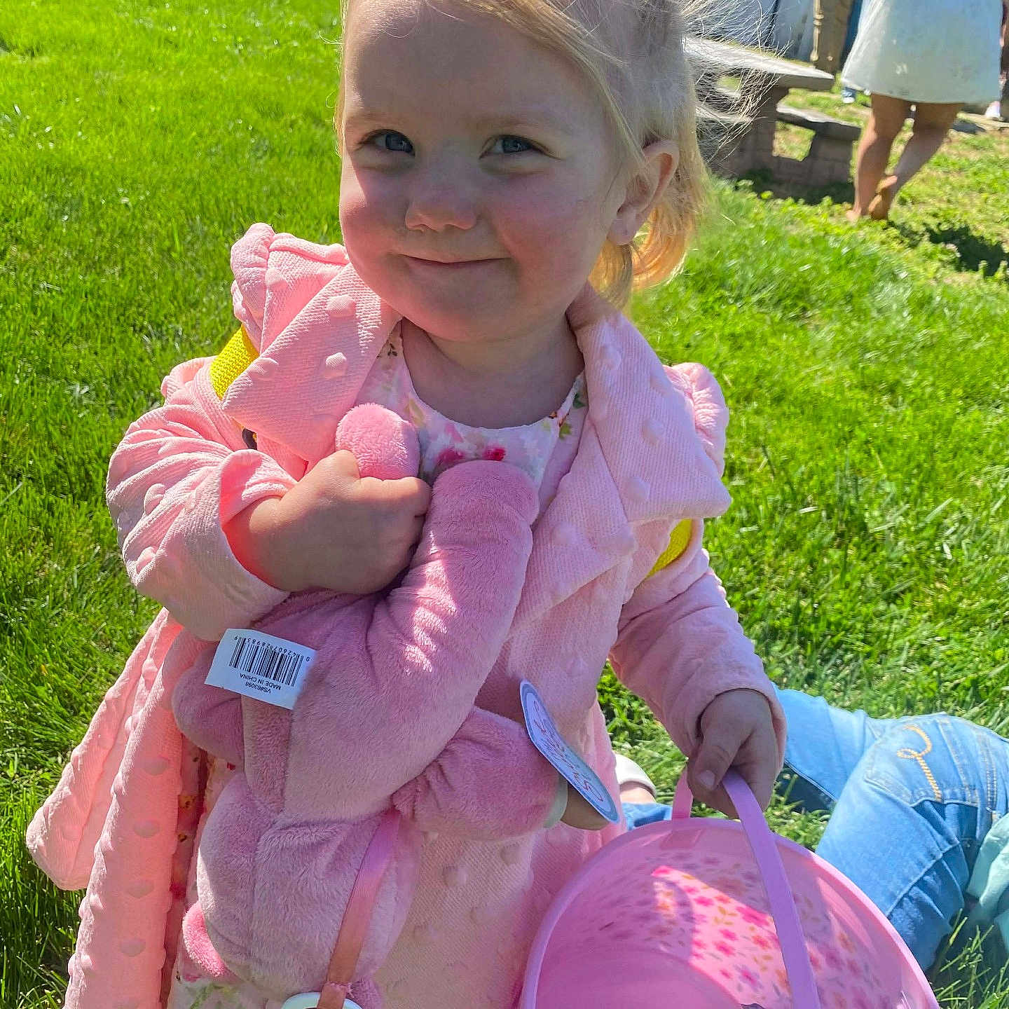 Ensleigh is registered to the contest to win money with this photo: child, girl, blonde_hair, pink_jacket, stuffed_animal, pink_bunny, basket, candy, grass, outdoor, sunlight, smile, toy, person, casual_clothing, daylight, greenery, people, background, happy