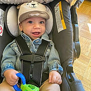 Leonidas joined the competition — help win amazing prizes! baby, child, smiling, hat, denim_jacket, car_seat, toy, straps, indoor, floor, wooden_floor, cute, happy, infant, clothing, seat, sitting, closeup, face, hand