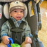 baby, child, smiling, hat, denim_jacket, car_seat, toy, straps, indoor, floor, wooden_floor, cute, happy, infant, clothing, seat, sitting, closeup, face, hand