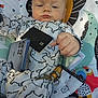 Lucus joined the competition — help win amazing prizes! baby, child, onesie, animal_print, smartphone, black_card, keys, play_mat, colorful, pattern, face, hand, infant, cute, relaxed, indoor, toy, accessory, person, portrait
