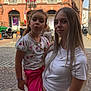 bracelet, building, child, cobblestone, daylight, flag, girl, historic_building, necklace, outdoor, person, pink_pants, pose, sky, smile, street, teenager, urban, white_shirt, window