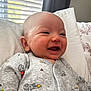 George is registered to the contest to win money with this photo: baby, infant, smiling, face, clothing, onesie, robot_pattern, pillow, indoor, window, curtain, happy, cute, child, portrait, skin, head, expression, cozy, lying_down