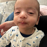 Eyan a rejoint le concours — aidez-le/la à gagner de superbes lots ! baby, blue_text, clothing, cute, expression, face, hand, head, holding, home, indoor, infant, onesie, person, seated, skin, sleepy, text_pattern, white_clothing, young_child