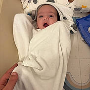 Eyan a rejoint le concours — aidez-le/la à gagner de superbes lots ! baby, towel, hand, face, wrapped, infant, blanket, soft, curious, open_mouth, patterned_mat, blue_brush, toy, white, skin, newborn, cute, indoors, child, person