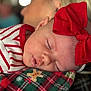 baby, sleeping, red_bow, striped_clothing, blanket, gingerbread_pattern, plaid_pattern, face, head, close_up, infant, person, resting, soft_lighting, holiday_theme, cozy, blurred_background, child, cute, peaceful