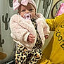 baby, pacifier, pink_jacket, headband, bow, leopard_print, pants, yellow_sweatshirt, hand, indoor, curtain, cactus_pattern, person, child, infant, cute, fashion, portrait, holding, cozy
