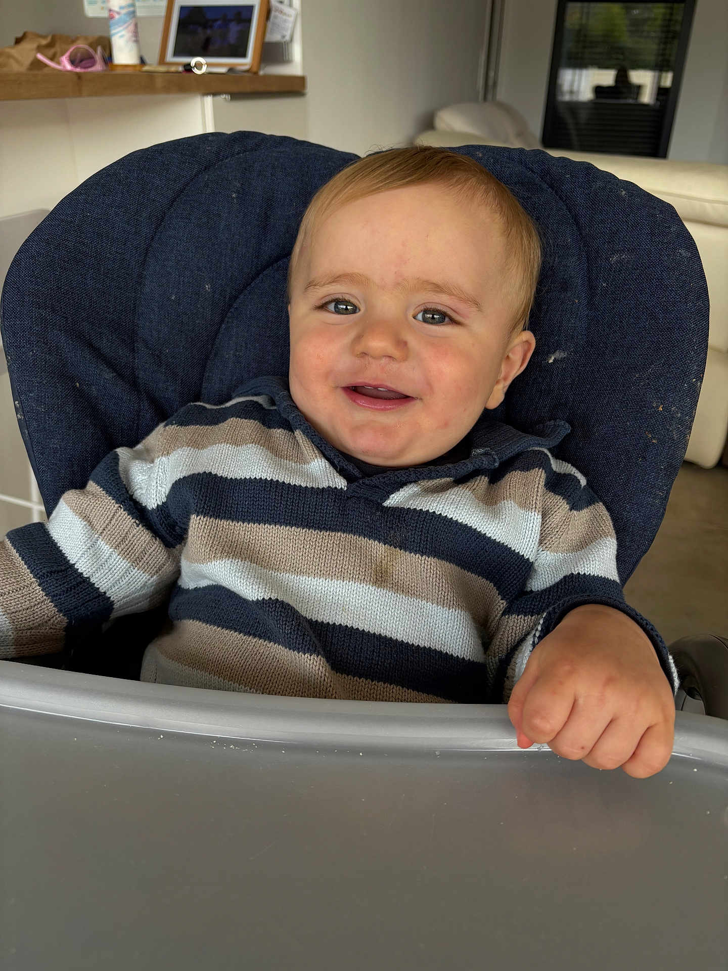 Oscar a rejoint le concours — aidez-le/la à gagner de superbes lots ! baby, child, high_chair, smile, striped_sweater, happy, indoor, face, hand, person, furniture, modern, living_room, cozy, cute, young_child, portrait, seated, expression, casual