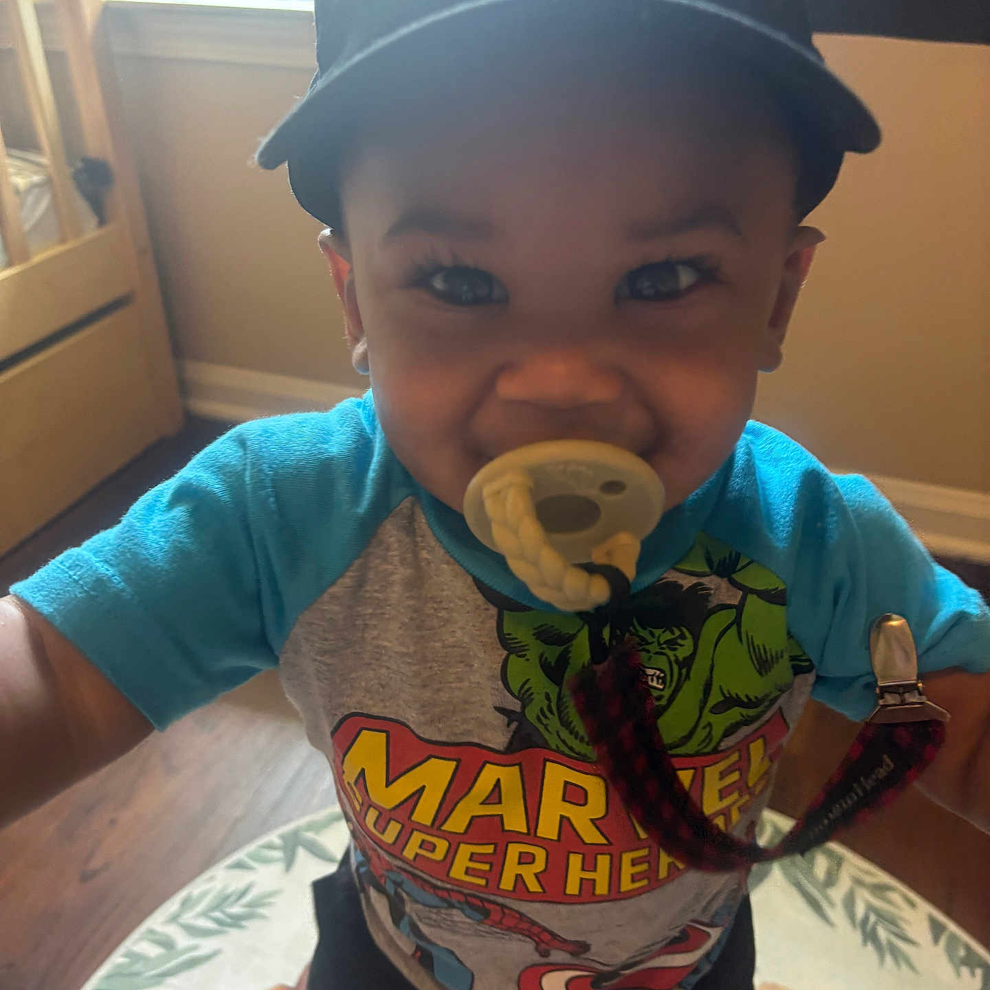 Kyrian joined the competition — help win amazing prizes! animal_print, baby, cap, child, clothing, cute, floor, happy, indoors, marvel, nike, pacifier, person, rug, shirt, smiling, superhero, toddler, window, wooden_floor
