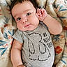Stiles is registered to the contest to win money with this photo: baby, child, infant, face, hand, blanket, clothing, onesie, cute, portrait, lying_down, expression, soft, cheeks, person, fabric, pattern, animal_illustration, text_on_clothing, indoor