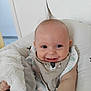 baby, smiling, hair_tuft, bib, plush_toy, cushion, indoor, child, happy, face, person, infant, clothing, cute, portrait, sitting, hand, soft_toy, white, comfort