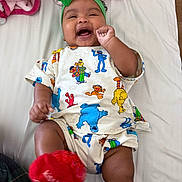 Daelani joined the competition — help win amazing prizes! baby, infant, smiling, laughing, green_headband, red_sock, sesame_street_clothing, bed, blanket, pink_blanket, happy, child, person, cute, indoor, lying_down, playful, colorful_clothing, head_accessory, footwear